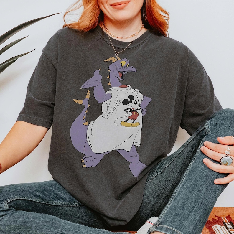 Peut inclure: T-shirt gris fonc&eacute; avec un dragon violet portant un t-shirt blanc avec un motif Mickey Mouse. Le dragon a des cornes jaunes et une longue queue. Le t-shirt est port&eacute; avec un jean bleu.