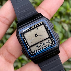 May include: Black Casio digital watch with a rectangular face. The watch displays the time as 4:06:42. The watch has a black strap and a blue accent around the face. The watch is water resistant.