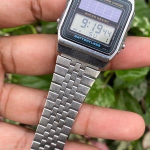 May include: A vintage Casio digital watch with a silver metal band. The watch face displays the time as 9:19:44 and the day as SU. The watch is labeled "WATER RESIST" and "BATTERYLESS".