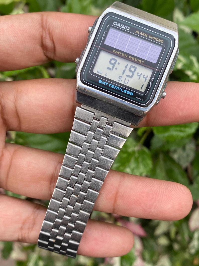 May include: A vintage Casio digital watch with a silver metal band. The watch face displays the time as 9:19:44 and the day as SU. The watch is labeled "WATER RESIST" and "BATTERYLESS".