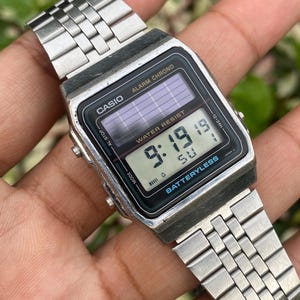 May include: A silver Casio digital watch with a black face displaying the time 9:19. The watch has a rectangular face, a metal band, and the text "CASIO" and "BATTERYLESS" are visible. The watch is a vintage style.