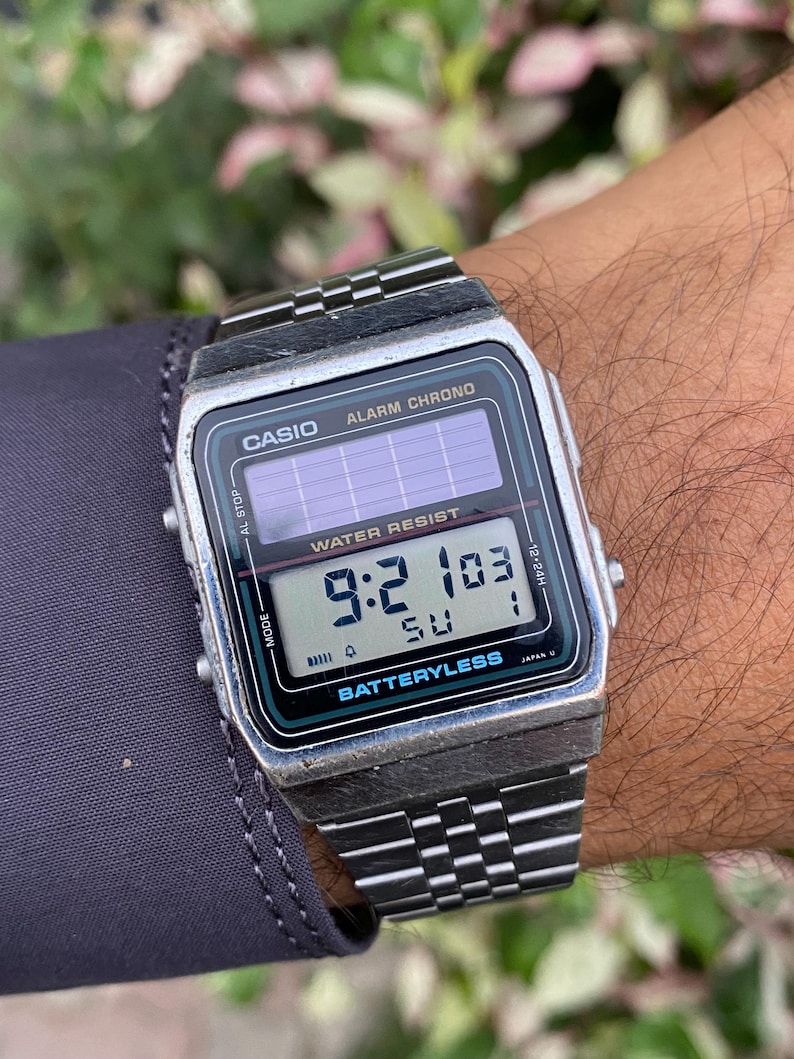 May include: A silver Casio digital watch with a black face displaying the time 9:21:03. The watch has a rectangular face with the words "CASIO", "ALARM CHRONO", and "WATER RESIST" printed on it. The watch band is silver.