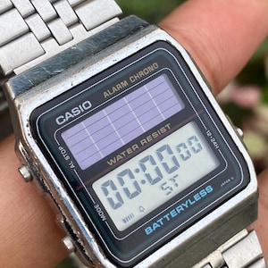 May include: A vintage Casio digital watch with a silver metal band. The watch face is black with a digital display showing "00:00 00". The watch has the text "CASIO", "ALARM CHRONO", and "BATTERYLESS".