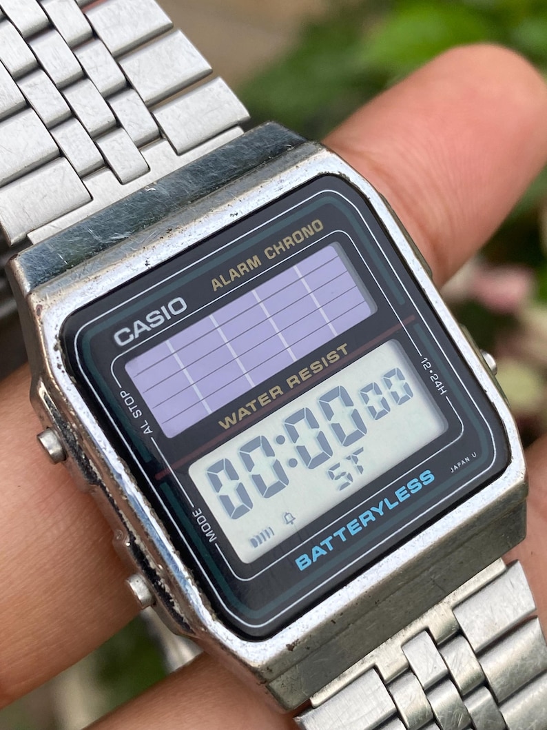 May include: A vintage Casio digital watch with a silver metal band. The watch face is black with a digital display showing "00:00 00". The watch has the text "CASIO", "ALARM CHRONO", and "BATTERYLESS".