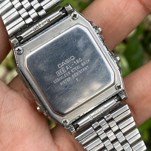 Może przedstawiać: Srebrny zegarek cyfrowy Casio AL-180, widok z tyłu. Tył ze stali nierdzewnej zawiera logo Casio i informacje o modelu. Pasek zegarka ma srebrny, połączony design.