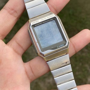 Puede incluir: Reloj digital Casio Hotbiz plateado con pantalla táctil y esfera rectangular. El reloj muestra la hora y la fecha. La correa está hecha de eslabones de metal plateado.