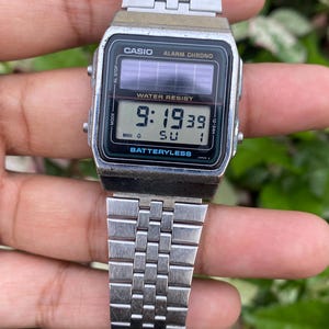 May include: A silver Casio digital watch with a rectangular black face displaying the time 9:19:39. The watch has a silver metal band and the text "CASIO" and "WATER RESIST" are visible on the face. The watch is battery-less.