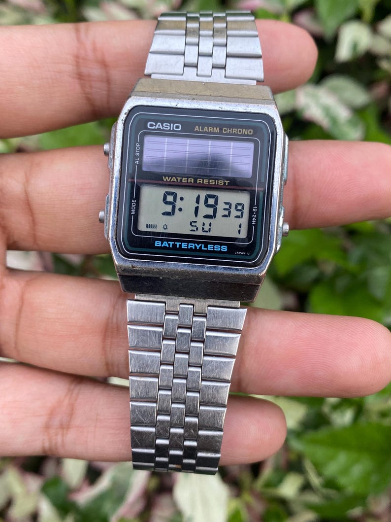 May include: A silver Casio digital watch with a rectangular black face displaying the time 9:19:39. The watch has a silver metal band and the text "CASIO" and "WATER RESIST" are visible on the face. The watch is battery-less.