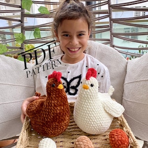 Peut inclure: Une jeune fille souriante tient un poulet crocheté marron et blanc, avec des crêtes rouges et des becs jaunes, dans un panier en osier. Le panier contient également trois œufs crochetés blancs, beiges et orange. Le texte "PDF PATTERN" est visible.