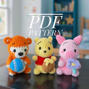May include: Three crocheted plush toys: an orange bear holding a blue ball, a yellow bear with a red shirt holding a honey pot, and a pink pig holding a flower. The text "PDF PATTERN" is displayed above the toys.