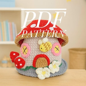 May include: A handmade crochet mushroom house with a red cap and white spots. It has pink and yellow flower windows, a brown door, and a yellow bee. The text "PDF PATTERN" is visible. The house is a charming, whimsical design.