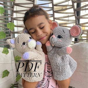 Op de afbeelding: Een jong meisje omhelst twee handgemaakte gehaakte dierenpoppen. Eén is lichtbeige met paarse accenten, de andere is grijs met roze oren. De tekst "PDF PATTERN" is zichtbaar op één pop.