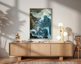 May include: A framed art print depicting a dramatic seascape with crashing waves and a rocky coastline. The artwork is displayed above a light wood cabinet, with a modern lamp and decorative objects.