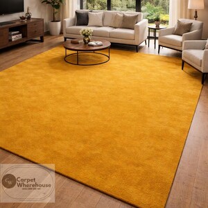 Könnte beinhalten: Ein großer, rechteckiger, goldgelber Teppich dominiert das Wohnzimmer. Der Teppich liegt auf einem Holzboden, und der Raum verfügt über ein Sofa, Stühle und einen Couchtisch in neutralen Tönen. Ein großes Fenster bietet einen Blick ins Freie.