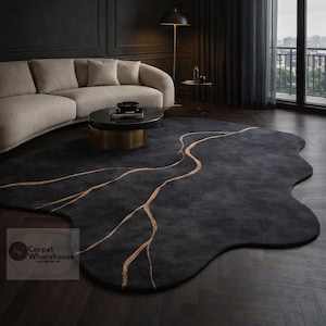 May include: A dark grey, organically shaped rug featuring a gold vein pattern. The rug is positioned on a dark wood floor within a contemporary living space. The distinctive form and contrasting hues of the rug contribute to a visually appealing focal point.