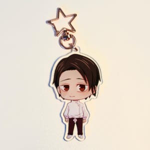 May include: A clear acrylic keychain with a chibi-style illustration of a person with dark brown hair and red eyes. The character wears a white shirt and dark purple trousers. The keychain has a star-shaped clasp.