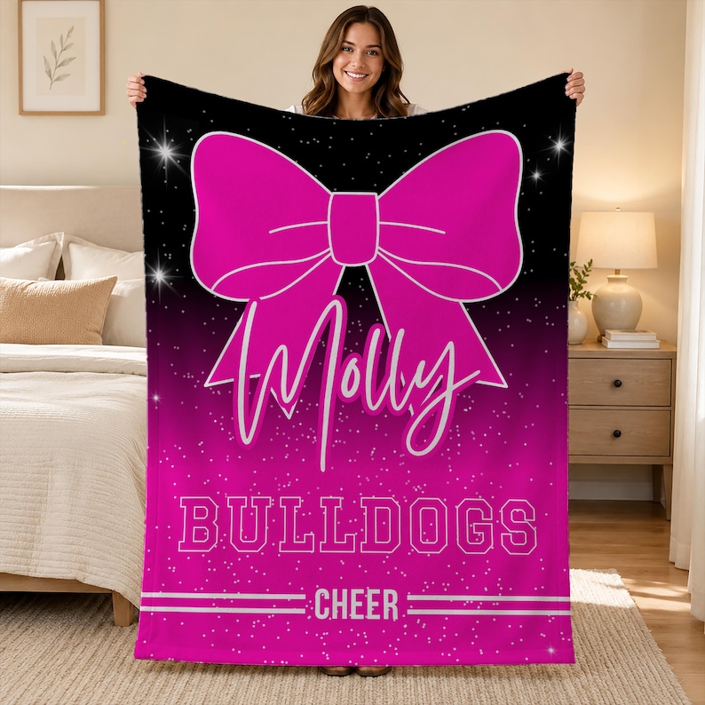 May include: A rectangular fleece blanket featuring a large hot pink bow graphic on a black and pink gradient background with white sparkles. The text Molly is written in a white script font, followed by the word BULLDOGS and the word CHEER.