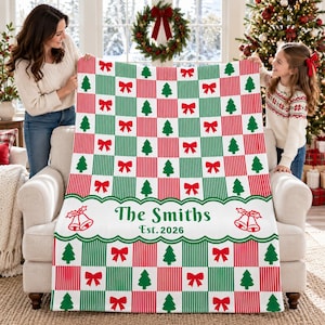 May include: A soft throw blanket featuring a checkered pattern of red and green stripes alternating with white squares containing red bows and green Christmas trees. A white horizontal band displays the text The Smiths Est. 2026.