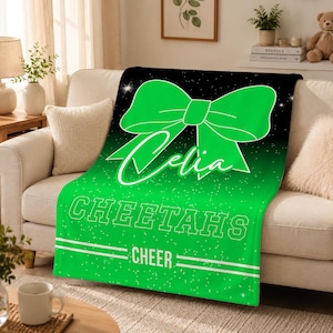 May include: A soft throw blanket featuring a large bright green bow graphic on a black and green gradient background with white glitter accents. The text Celia is written in script, followed by the block text CHEETAHS and the word CHEER.