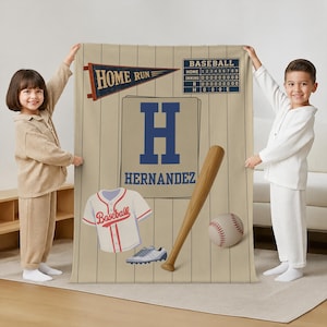 May include: A beige baseball-themed blanket featuring a pinstripe pattern, a blue letter H, the name HERNANDEZ, a HOME RUN pennant, a scoreboard, a white baseball jersey with red trim, a baseball bat, a baseball, and a pair of athletic cleats.