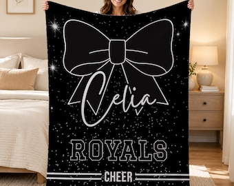 Può includere: Una coperta rettangolare nera in pile con un grande contorno bianco di un fiocco nella parte superiore. Il nome Celia è stampato in corsivo bianco sotto il fiocco. Il testo ROYALS è in stampatello bianco, seguito dalla parola CHEER e da linee.