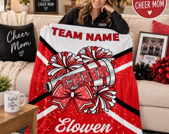 Può includere: Una coperta in pile bianca e rossa con il testo TEAM NAME ed Elowen, raffigurante un megafono, un grande fiocco e dei pon-pon. Il design presenta strisce diagonali nere e una texture rossa glitterata sugli elementi a tema cheerleading.