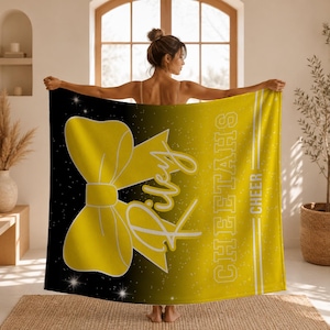 May include: A rectangular fleece blanket featuring a black to yellow gradient background with a sparkling star effect. A large yellow cheer bow graphic is on the left, with the name Riley in white script and the text CHEETAHS CHEER in white block letters.