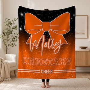 May include: A rectangular fleece blanket featuring a black-to-orange gradient background with white sparkles. A large orange bow graphic sits above the white script text Molly, the block text CHEETAHS, and the word CHEER between two horizontal lines.