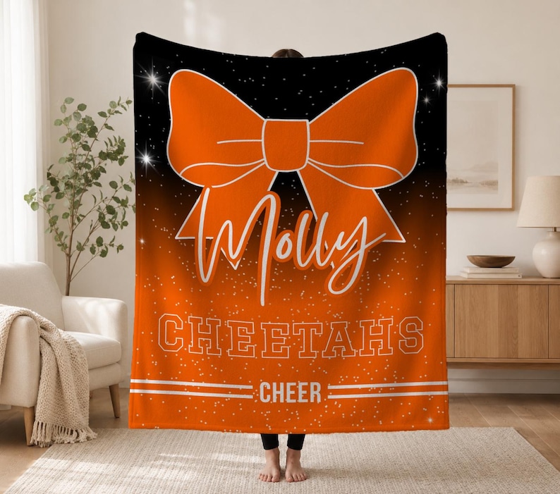 May include: A rectangular fleece blanket featuring a black-to-orange gradient background with white sparkles. A large orange bow graphic sits above the white script text Molly, the block text CHEETAHS, and the word CHEER between two horizontal lines.