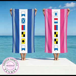 May include: Two rectangular beach towels, one blue and one pink, each featuring a central white vertical stripe decorated with a series of six colorful nautical signal flags. The towels have white vertical pinstripes along the outer edges.