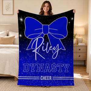May include: A rectangular fleece blanket featuring a black and blue gradient background with a white speckled star pattern. A large blue bow graphic is centered above the white script name Riley, the word DYNASTY, and the word CHEER.