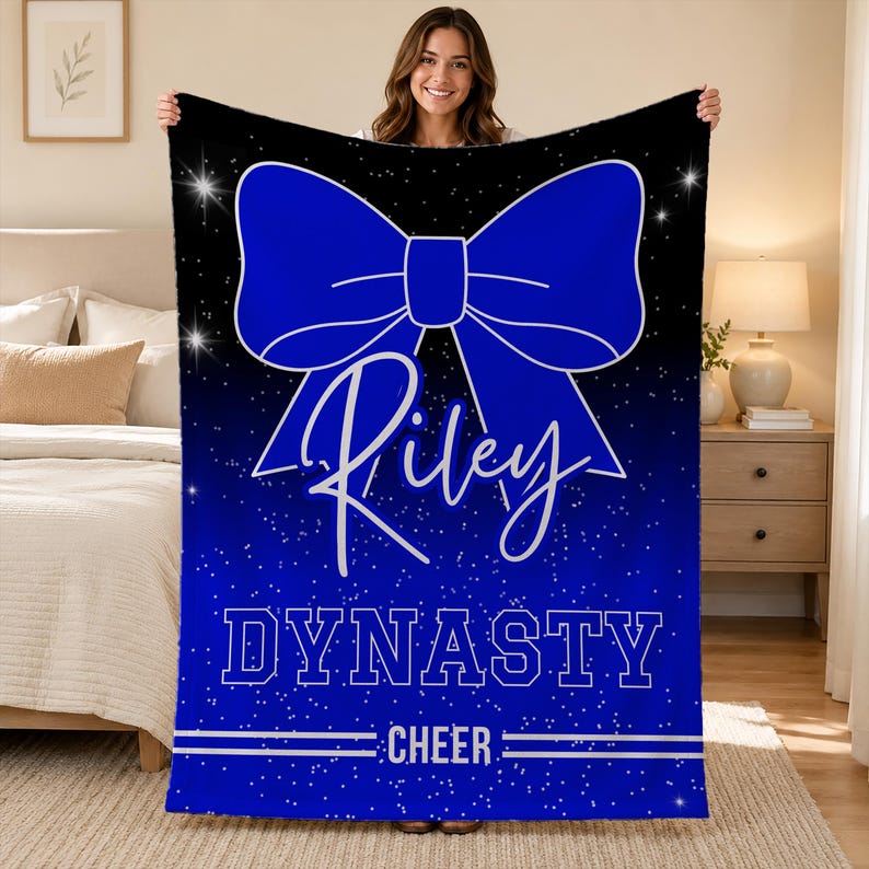 May include: A rectangular fleece blanket featuring a black and blue gradient background with a white speckled star pattern. A large blue bow graphic is centered above the white script name Riley, the word DYNASTY, and the word CHEER.