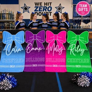 May include: Four rectangular towels featuring large bows and personalized names: Celia in blue, Emma in purple, Molly in pink, and Riley in green. Each towel displays a glittery gradient background, the team name Bulldogs or Cheetahs, and the word Cheer.