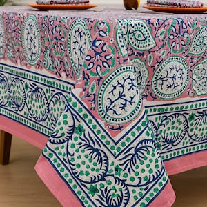Könnte beinhalten: Eine rechteckige Tischdecke mit rosafarbenem Hintergrund und einem sich wiederholenden Muster aus blauen und grünen Blumen- und Paisley-Motiven. Das Design umfasst einen breiten Rand mit blau-grünem Blumenmuster und einen einfarbigen rosa Saum.