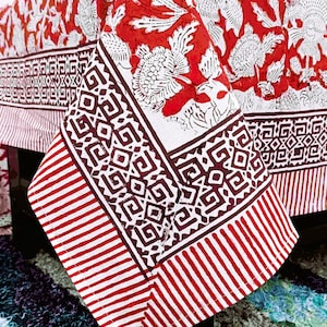 Könnte beinhalten: Eine rot-weiß gemusterte Tischdecke mit geometrischem Rand. Die Tischdecke ist über einen Tisch drapiert und zeigt das komplizierte Design und Farbschema. Der Stoff hat einen gestreiften Rand.