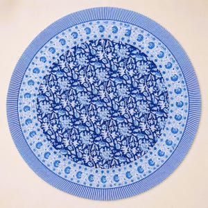 Könnte beinhalten: Ein runder Tischläufer mit blauem und weißem Blumenmuster. Die Mitte zeigt ein dichtes Blumenmuster, umgeben von einem Rand aus stilisierten Blumen und einem gestreiften Rand. Der Tischläufer ist eine lebendige Ergänzung für jede Tischdekoration.