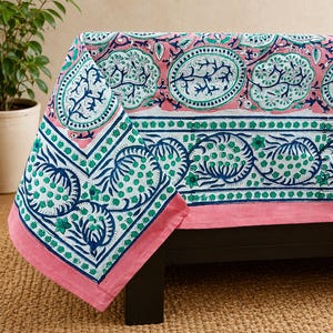 Könnte beinhalten: Eine rechteckige Tischdecke mit einem Blockdruckmuster in den Farben Rosa, Grün und Dunkelblau. Das Design umfasst ovale Motive mit baumartigen Formen, florale Elemente und eine breite Bordüre mit sich wiederholenden botanischen Mustern.