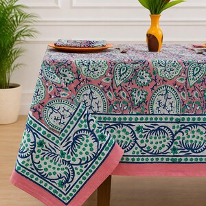 May include: A rectangular tablecloth featuring a pink background with a repeating pattern of blue and green floral motifs. The fabric has a wide border with a darker blue and green botanical design, finished with a solid pink hem along the edges.