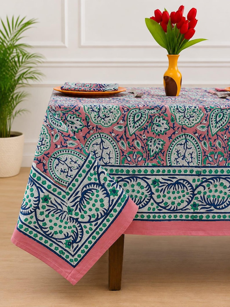 May include: A rectangular tablecloth featuring a pink background with a repeating pattern of blue and green floral motifs. The fabric has a wide border with a darker blue and green botanical design, finished with a solid pink hem along the edges.