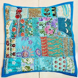 Könnte beinhalten: Quadratisches Zierkissen mit Patchwork-Design. Das Kissen hat eine Vielzahl von Stoffen in Blau-, Türkis- und Goldtönen mit Blumen- und Paisley-Mustern. Es hat einen durchgehenden blauen Rand.