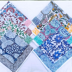 Könnte beinhalten: Eine Sammlung gefalteter quadratischer Stoffservietten mit verschiedenen Blumen- und Paisley-Mustern. Die Servietten weisen eine Reihe von Farben auf, darunter Blau, Rosa, Grün und Gelb, mit weißen Hintergründen und gemusterten Rändern.