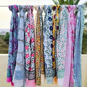 Könnte beinhalten: Eine Sammlung farbenfroher, gemusterter Schals, die an einer Stange hängen. Die Schals zeigen verschiedene Blumen- und geometrische Designs in Rosa, Blau, Gelb und Weiß. Die Schals sind aus leichtem Stoff gefertigt.