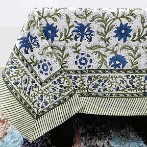 Może przedstawiać: Biały obrus z niebieskim wzorem kwiatowym i zielonymi winoroślami. Obramowanie ma wzór w paski w kolorze zielonym i białym. Obrus jest wykonany z miękkiego materiału, prawdopodobnie bawełny.