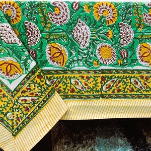 Könnte beinhalten: Eine grüne und weiße Tischdecke mit Blumenmuster und gelben und roten Akzenten. Die Tischdecke hat ein sich wiederholendes Muster aus Blumen und Blättern mit einem gelb-roten Rand. Die Kanten sind mit einem gelb-weiß gestreiften Muster versehen.