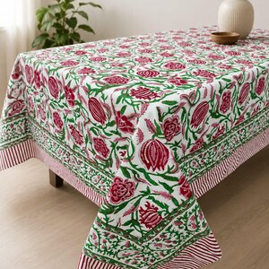 May include: A rectangular tablecloth featuring a white base with a repeating floral pattern in deep magenta and green. The design includes stylized flowers and buds, finished with a decorative border of green vines and a thin red and white striped edge.