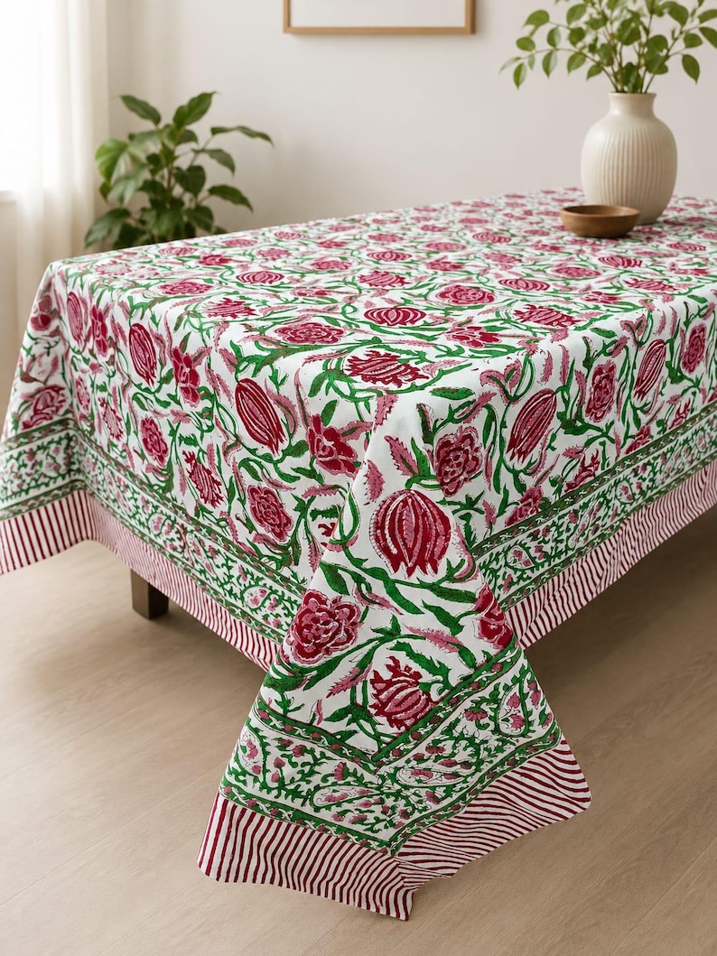 May include: A rectangular tablecloth featuring a white base with a repeating floral pattern in deep magenta and green. The design includes stylized flowers and buds, finished with a decorative border of green vines and a thin red and white striped edge.