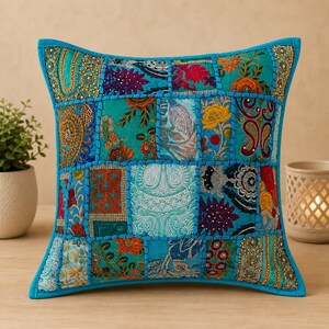 Könnte beinhalten: Ein quadratisches Zierkissen mit einem Patchwork-Design aus verschiedenen türkisfarbenen, blauen und bunten Stoffquadraten. Jedes Quadrat zeigt aufwendige Stickereien, florale Muster und Metallperlen, die durch dicke türkisfarbene Nähte verbunden sind.