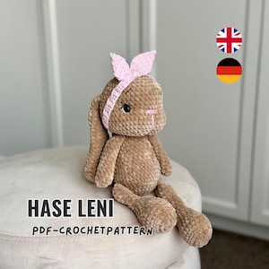 May include: A brown plush rabbit toy with long ears and a pink crocheted headband. The rabbit has embroidered eyes and a pink nose. Text on the image reads HASE LENI PDF-CROCHETPATTERN. The toy is made of soft, textured yarn material.