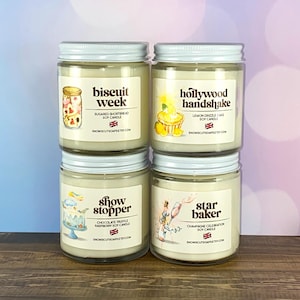 May include: Four glass jar candles with white labels and silver lids. The labels read "biscuit week", "hollywood handshake", "show stopper", and "star baker". Each label has a unique illustration and the text "soy candle".