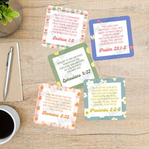 Può includere: Una collezione di biglietti quadrati con citazioni ispiratrici dalla Bibbia. Ogni biglietto presenta un versetto diverso, illustrazioni floreali e di frutta e una combinazione di colori unica. I biglietti sono disposti su una superficie di legno.